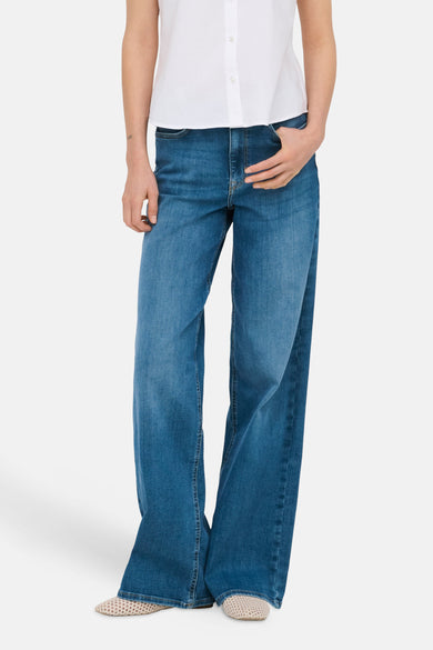 Jean large MADISON BLUSH bleu moyen en denim de ONLY, avec une main dans la poche, et une chemise blanche.