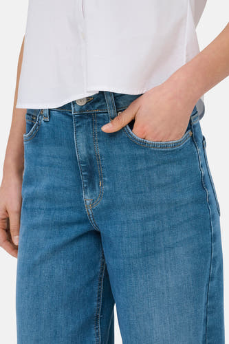 MADISON BLUSH mid blue denim wide jeans van ONLY, met een hand in de zak, en een wit overhemd.

