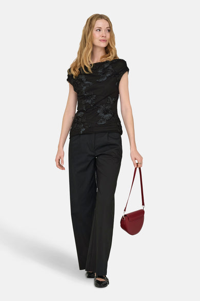 Zwarte blouse met korte mouwen van JDY, met bloemmotief en gedragen met zwarte broek en rode handtas.
