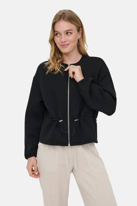 Zwarte korte jas van ONLY® met rits aan de voorkant en trekkoord in de taille, gedragen met een beige broek.
