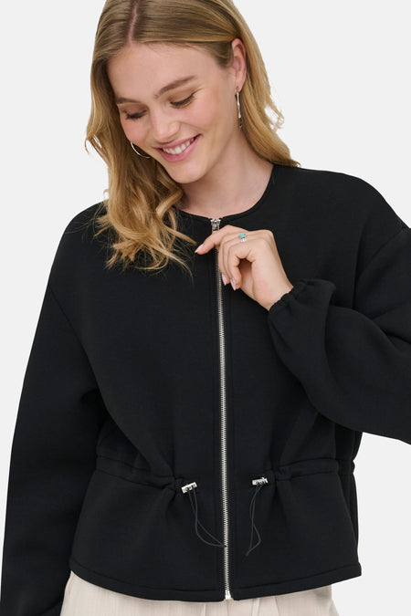 Zwarte korte jas van ONLY® met ronde hals, volledige rits en trekkoord in de taille, gedragen door een lachende vrouw.