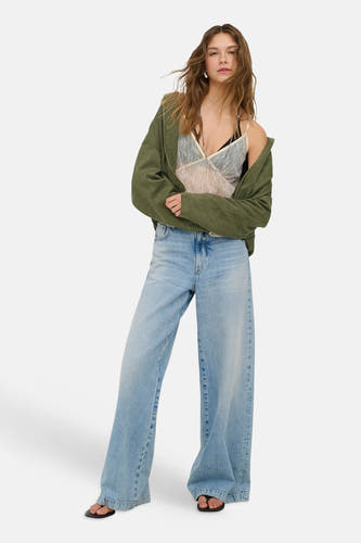 Ecru kanten blouse van ONLY® met spaghettibandjes, gedragen onder een open groen jack en wijde jeans.