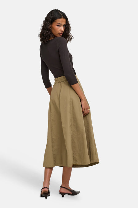 Bruine lange mouwen t-shirt van JDY, ribstructuur, strak model, zijprofiel van model met groene rok en zwarte sandalen