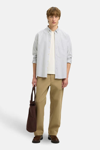 Chemise blanche à carreaux à manches longues de SELECTED portée sur un T-shirt blanc, associée à un pantalon kaki et une sac marron.