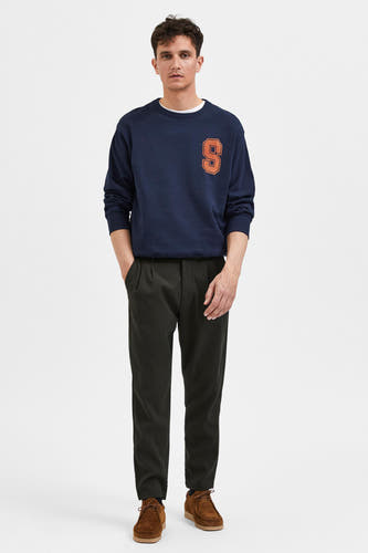 Groene broek van SELECTED, gecombineerd met een donkerblauwe sweater en bruine schoenen.