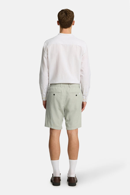Groene short van SELECTED, met achterzakken en gedragen met een wit overhemd, sokken en schoenen.
