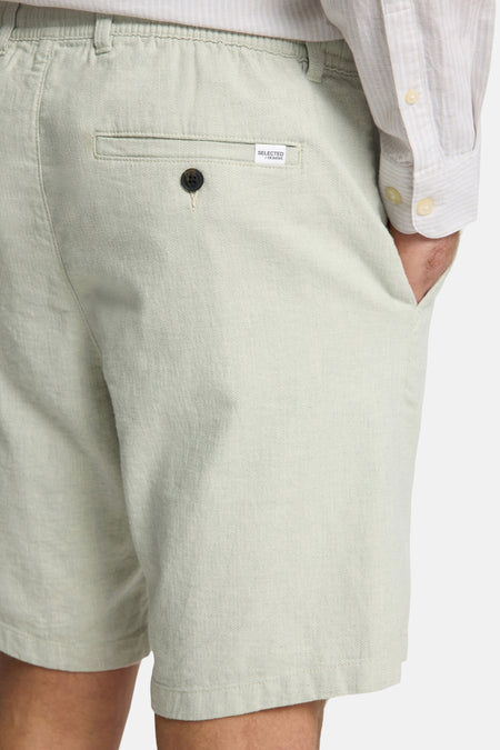 Groene short van SELECTED / HOMME, met een knoopdetail en een steekzak, in close-up.
