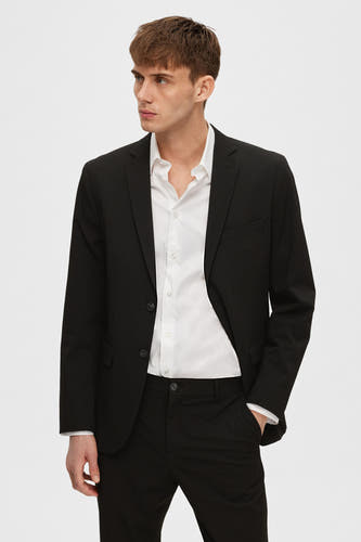 Zwarte blazer van SELECTED, met een witte overhemd en zwarte pantalon, model met hand in zak.