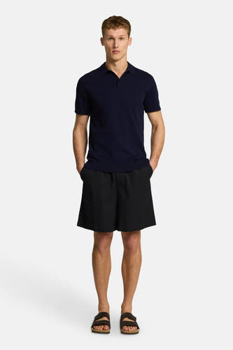 Blauwe polo met korte mouwen van SELECTED, gedragen met zwarte shorts en bruine sandalen.
