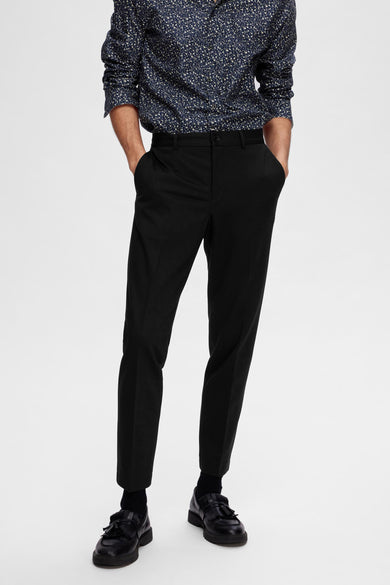 Zwarte kostuumbroek van SELECTED, gedragen met een blauw bloemen overhemd en zwarte loafers.
