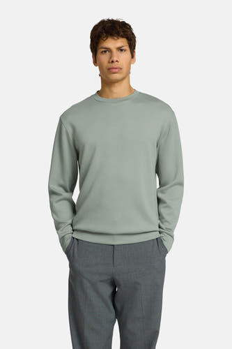 Groene sweater met ronde hals van SELECTED, gedragen door een man met handen in zakken en een grijze broek.