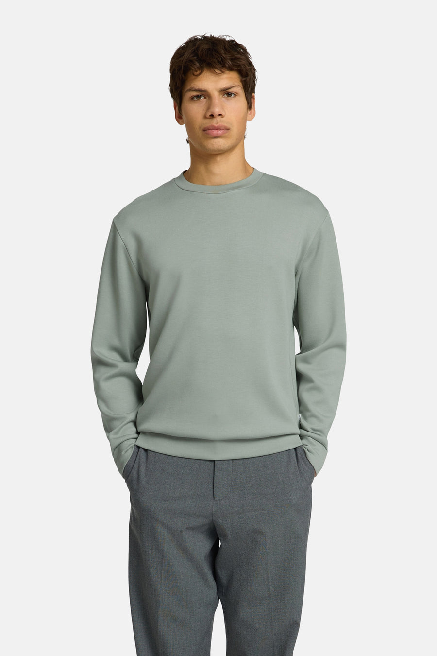 Groene sweater met ronde hals van SELECTED, gedragen door een man met handen in zakken en een grijze broek.