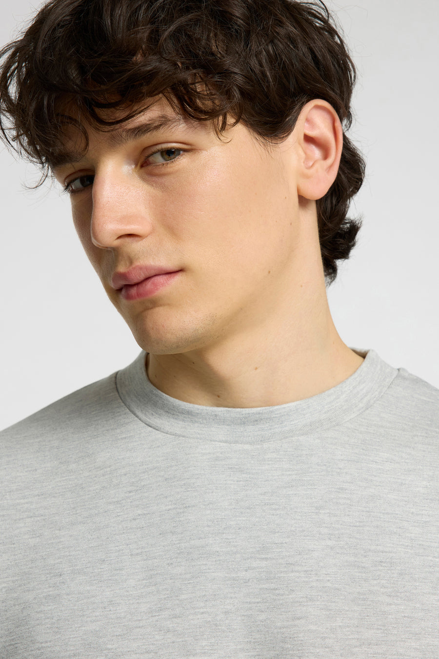 Pull gris à col rond de SELECTED, gros plan sur le visage d'un homme aux cheveux bruns foncés et bouclés.