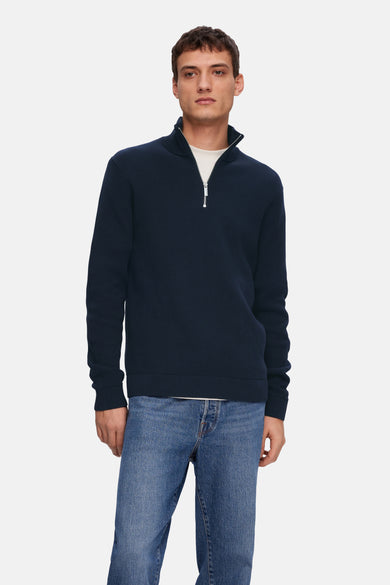 Blauwe trui van SELECTED, met een rits en gedragen over een wit T-shirt en een blauwe jeans.
