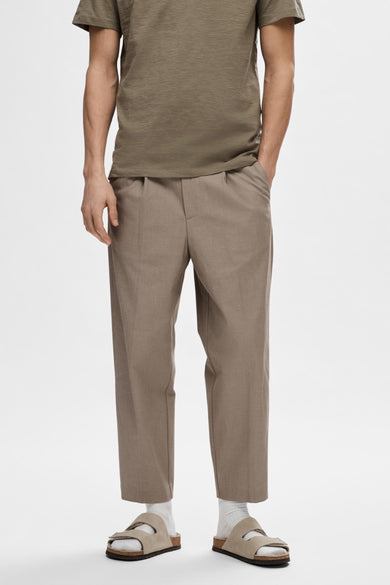 Jean beige de SELECTED, plissé, porté avec un T-shirt vert olive et des sandales en cuir avec des chaussettes blanches.