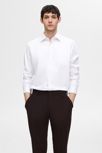 Wit overhemd met lange mouwen van SELECTED, gedragen met een donkere pantalon, met de handen in de zakken.
