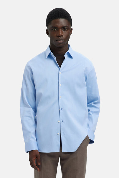 Blauw overhemd met lange mouwen van SELECTED, met knoopsluiting en gedragen met een bruine broek.
