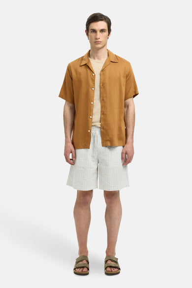 Chemise beige à manches courtes de SELECTED, portée sur un T-shirt beige et des short rayés, avec des sandales brunes.
