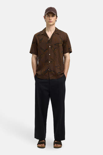 Chemise brune à manches courtes de SELECTED, imprimée de feuilles, portée avec un pantalon noir et des sandales.