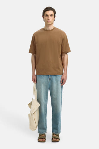 Bruin T-shirt met korte mouwen van SELECTED, gedragen met blauwe jeans, sandalen en een beige canvas tas.
