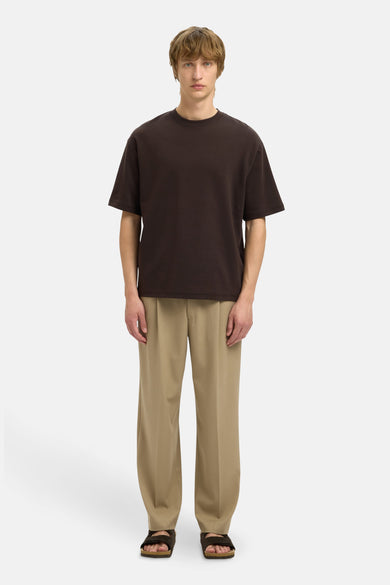 T-shirt marron à manches courtes de SELECTED, porté avec un pantalon beige et des sandales marrons.