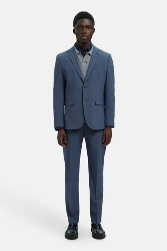 Blazer bleu de SELECTED, avec une subtile texture, associé à un gilet gris et à une chemise bleu marine, porté avec des chaussures noires.