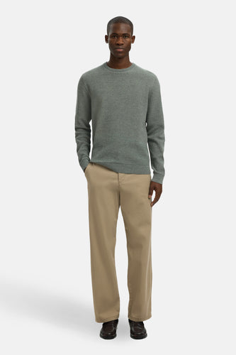 Man in groene trui en beige broek.