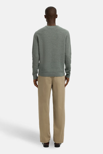 Achterkant van een man in een grijze trui en beige broek.