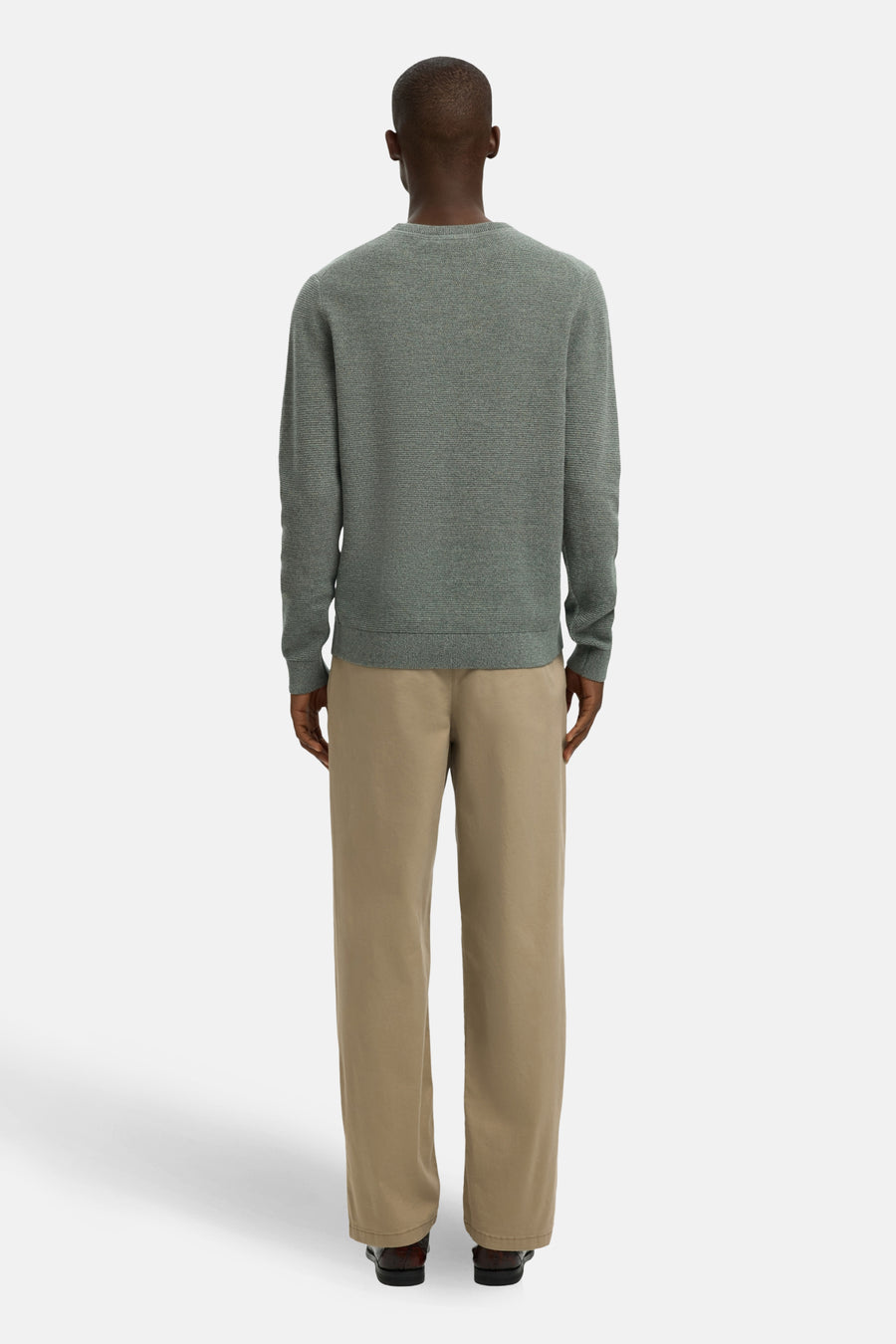 Achterkant van een man in een grijze trui en beige broek.