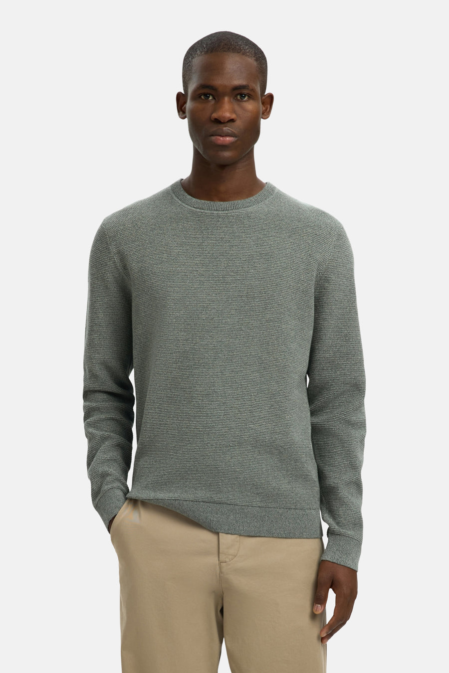 Een man in een grijze trui en beige broek.