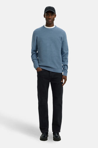 Blauwe ronde-halstrui van SELECTED, gedragen met een zwarte broek en een pet.

