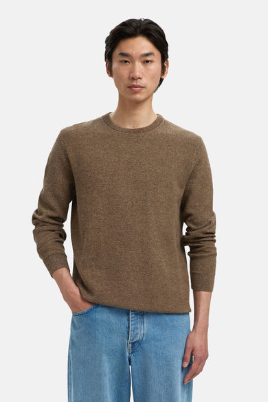 Bruine trui met ronde hals van SELECTED, gedragen met een blauwe jeans en een hand in de zak.

