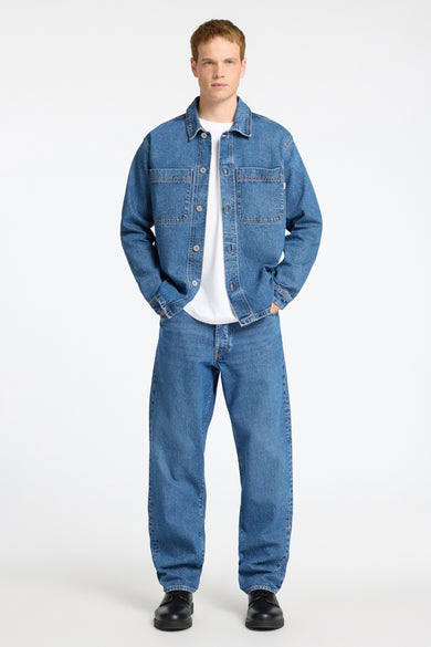 Jeanshemd in middenblauw denim van SELECTED, gedragen over een wit T-shirt, met bijpassende jeans en zwarte schoenen.
