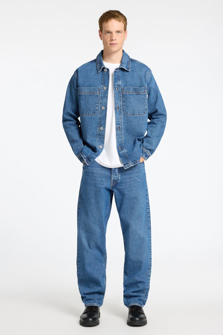 Jeanshemd in middenblauw denim van SELECTED, gedragen over een wit T-shirt, met bijpassende jeans en zwarte schoenen.
