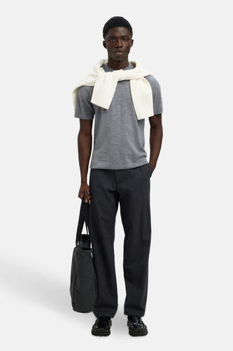 Grijze trui van SELECTED, gedragen met een witte trui over de schouders, gecombineerd met donkere broek en tas.
