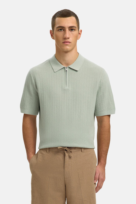 Polo verte SELECTED de couleur verte, à manches courtes et avec une fermeture éclair sur le devant, portée avec un short marron et des sandales.