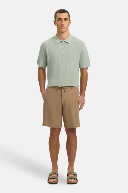 Groene polo van SELECTED, met korte mouwen en een ritssluiting aan de voorkant, gedragen met bruine shorts en sandalen.
