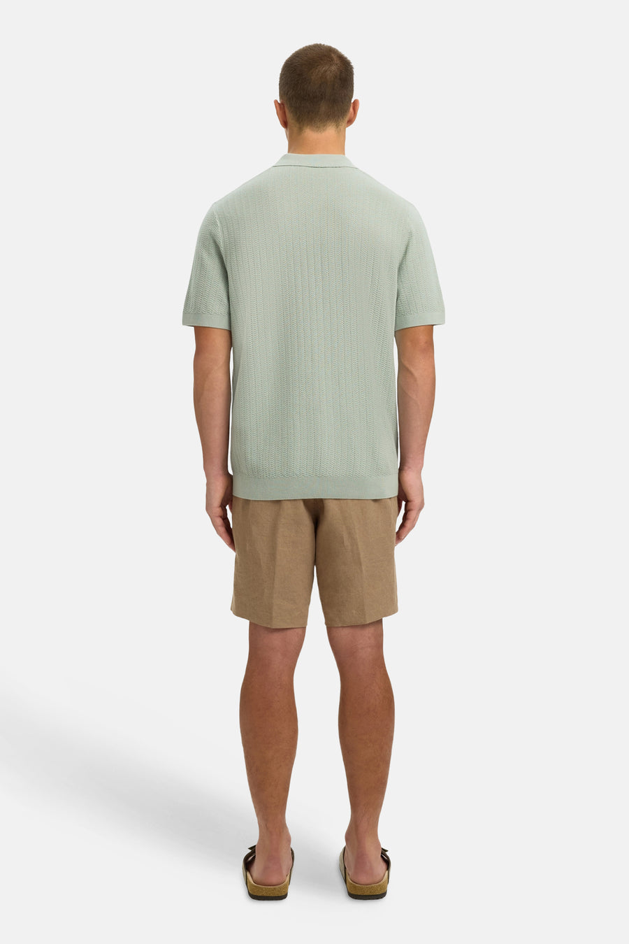 Polo verte SELECTED de couleur verte avec un motif à fines rayures, portée avec un short marron et des sandales.