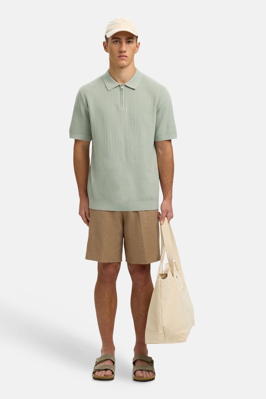 Polo verte SELECTED de couleur verte avec fermeture éclair, combinée avec un short beige et un sac en toile de couleur crème.