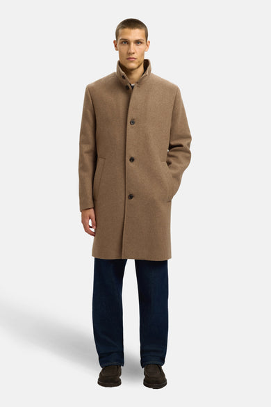 Lange bruine jas van SELECTED, met knoopsluiting en steekzakken, gecombineerd met een donkerblauwe jeans en bruine schoenen.