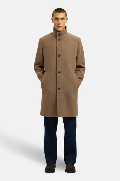 Bruine lange jas van SELECTED, met knoopsluiting en steekzakken, gedragen over donkere jeans en donkerbruine schoenen.
