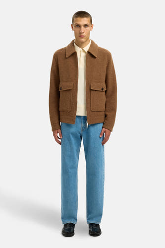 Bruine korte jas van SELECTED, met opgestikte zakken en gedragen over een crèmekleurige polo en blauwe jeans.
