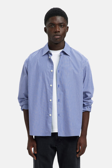 Blauw gestreept overhemd met lange mouwen van SELECTED, met witte strepen, gedragen over een wit T-shirt en zwarte broek.
