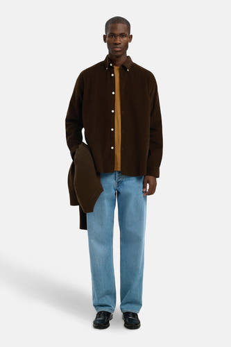 Bruin overhemd met lange mouwen van SELECTED, met een bruine trui in de hand en lichtblauwe jeans.

