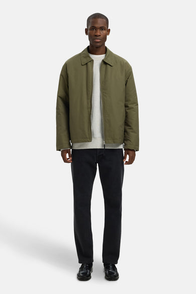 Pull-over gris avec col rond de SELECTED, porté sous un blouson vert olive et associé à des jeans noirs et des mocassins en cuir.