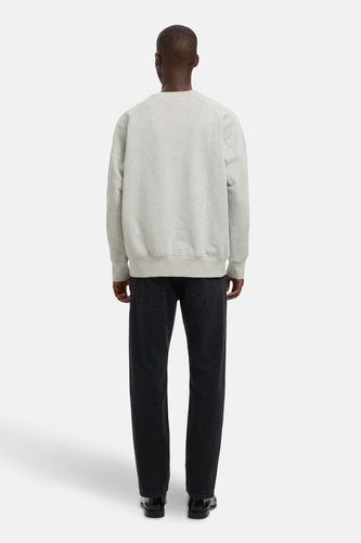 Achterkant van een man in grijze sweater, zwarte jeans en zwarte schoenen, staand tegen een witte achtergrond.