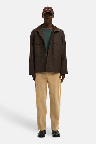 Bruine broek van SELECTED, met ribfluweeltextuur, gedragen met een bruin jasje en een groene trui.