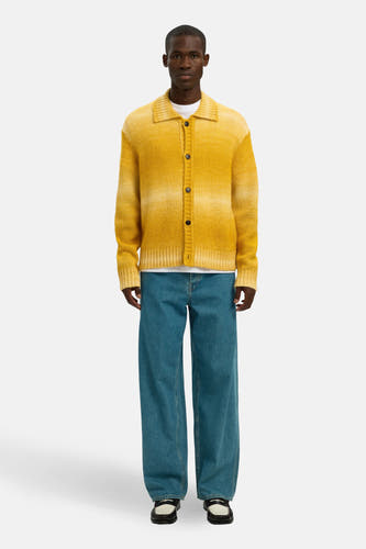 Geel vest van SELECTED, gedragen met een wit T-shirt en wijde blauwe jeans met zwarte leren loafers.
