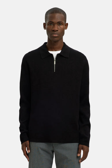 Zwarte trui met ronde hals van SELECTED, met een zilverkleurige rits en een witte T-shirt eronder, gedragen met een grijze pantalon.