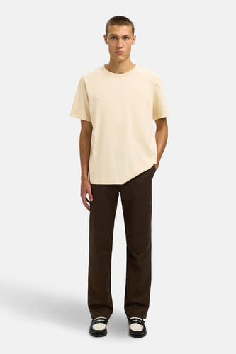Beige T-shirt met korte mouwen van SELECTED, gecombineerd met bruine pantalon en leren loafers.
